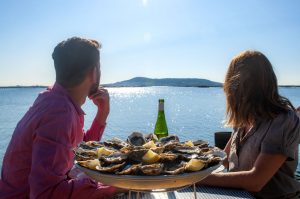 Couple de jeunes en train de boire un verre de vin et manger des huîtres au Petit Mas Loupian, au bord de l'Etang de Thau ©D.Cavailhes