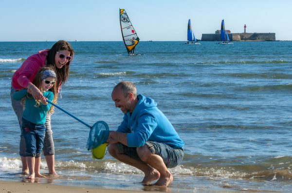 Une famille avec un enfant, en train de ramasser des crabes au bord de la mer, devant le fort Brescou au Cap d'Agde