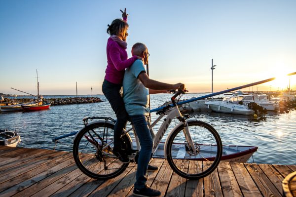 Un couple quinca jeuniors à vélo observent le coucher du soleil sur le port de Bouzigues au bord de l'étang de Thau