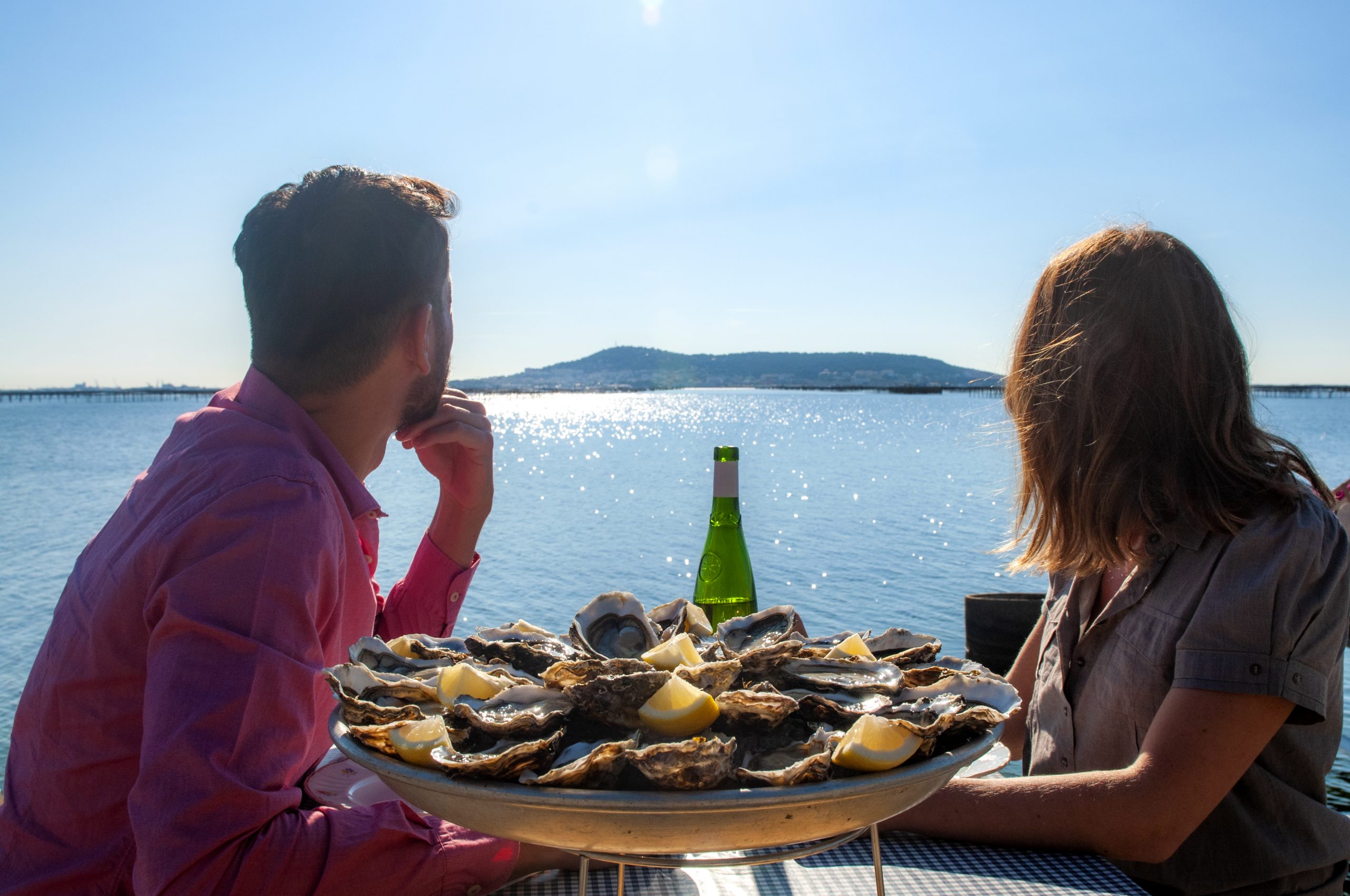 Un couple déjeune au bord du bassin de Thau en regardant Sète @D Cavailhes