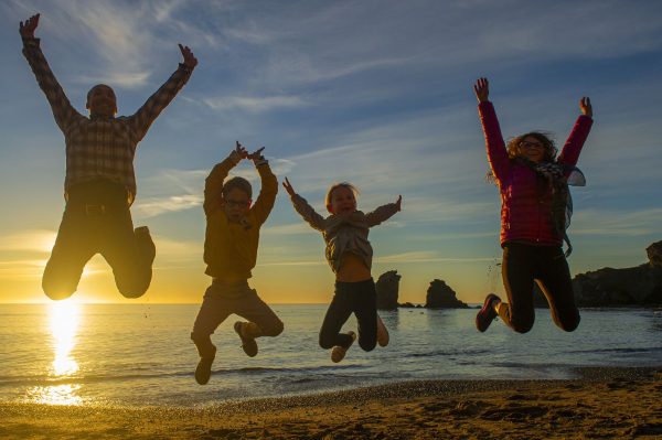 Une famille avec deux enfants qui s'amusent et qui sautent sur la plage au coucher du soleil