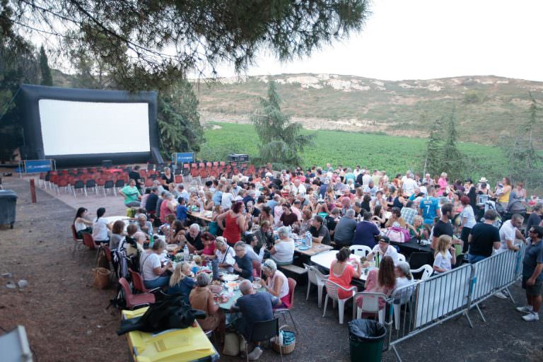 Projection de film au Festival Emmuscades au Mas Rimbaud à Frontignan avec de nombreuses personnes attablées et des vignes en arrière-plan