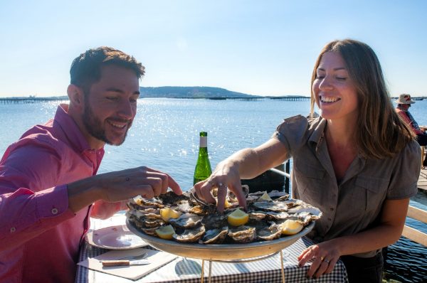 Un couple de jeunes, en train de manger des huîtres dans un mas conchylicoles, le petit Mas à Loupian, avec l'étang de Thau juste à côté
