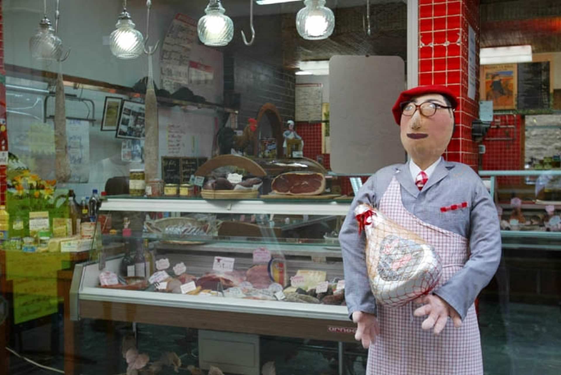 Petetas de Murviel Lès Béziers - Poupée de chiffon à taille humaine représentant un boucher avec tablier et jambon dans les mains devant la boucherie du village