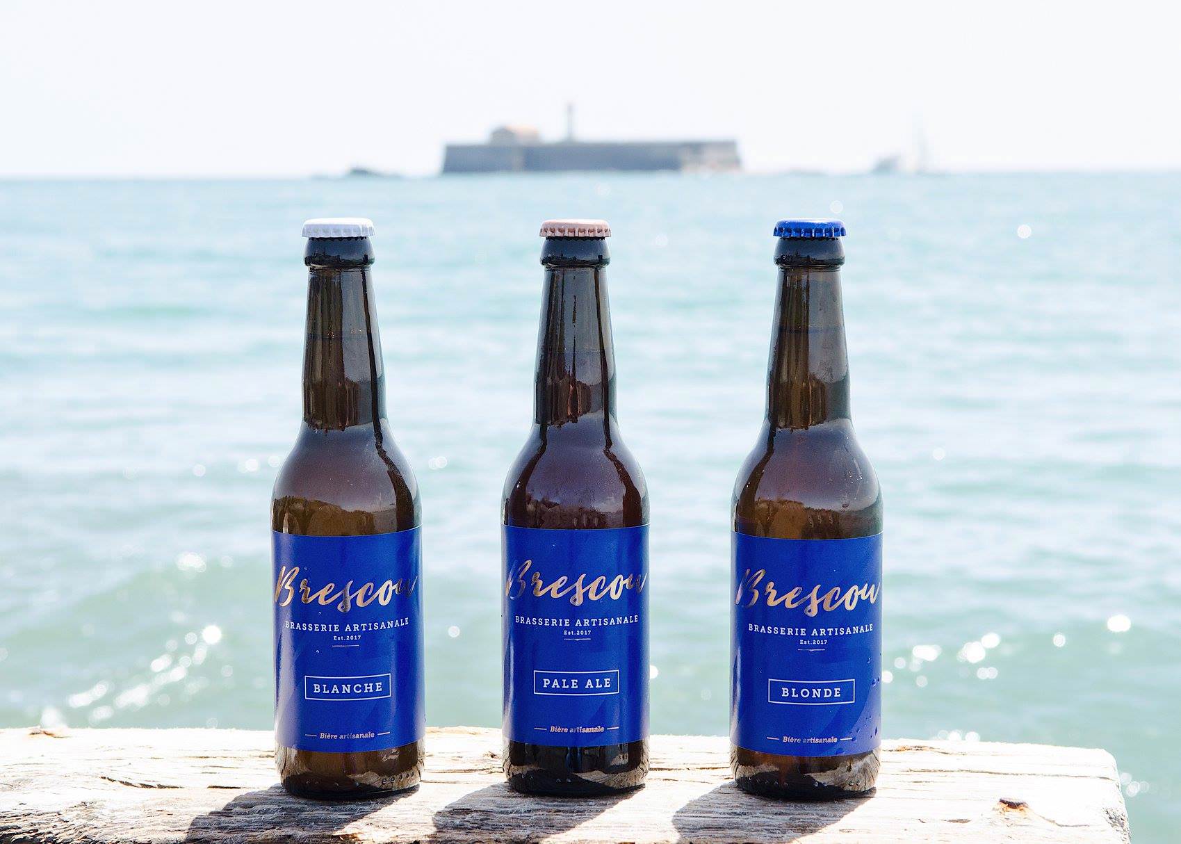 3 bouteilles de bières, avec en arrière plant le Fort de Brescou, fabriquées par la Brasserie Artisanale Brescou - Cap d'Agde