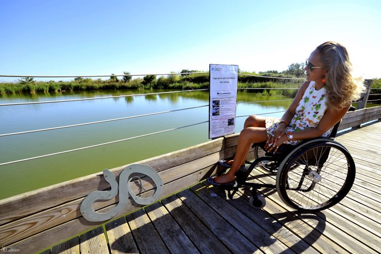 Une jeune femme en fauteuil observe l'étang du Méjean