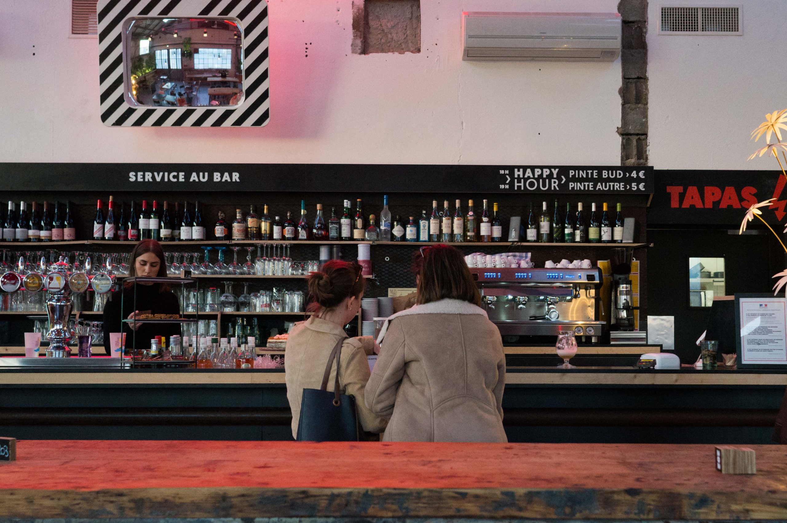 2 femmes de dos devant un bar garni de nombreuses bouteilles à La Halle Tropisme