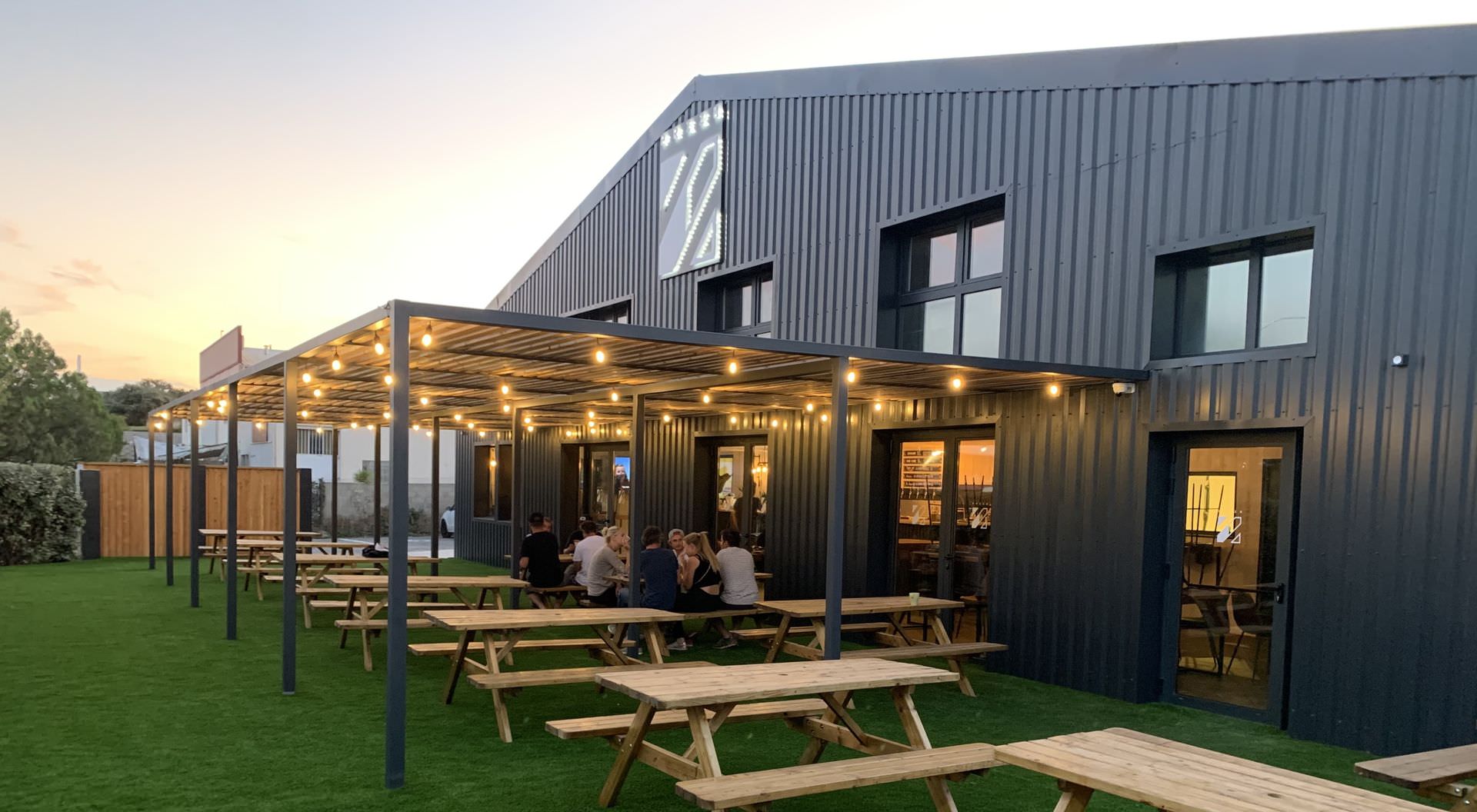 Terrasse extérieure couverte, grandes tables en bois, Vendargues, Prizm Brewing Co