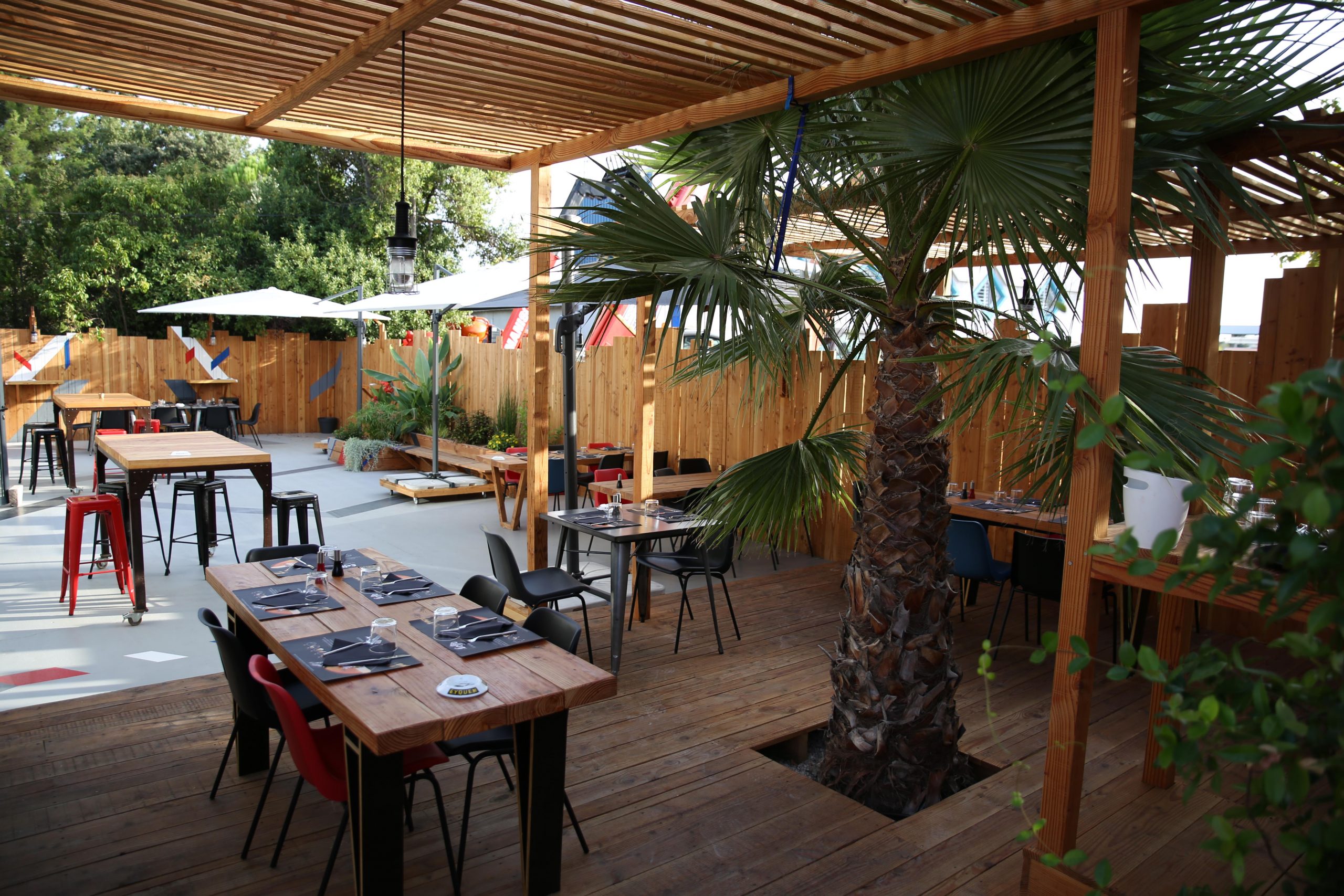 Grandes tables, et palmier, terrasse extérieure du Pro Race Café au Crès