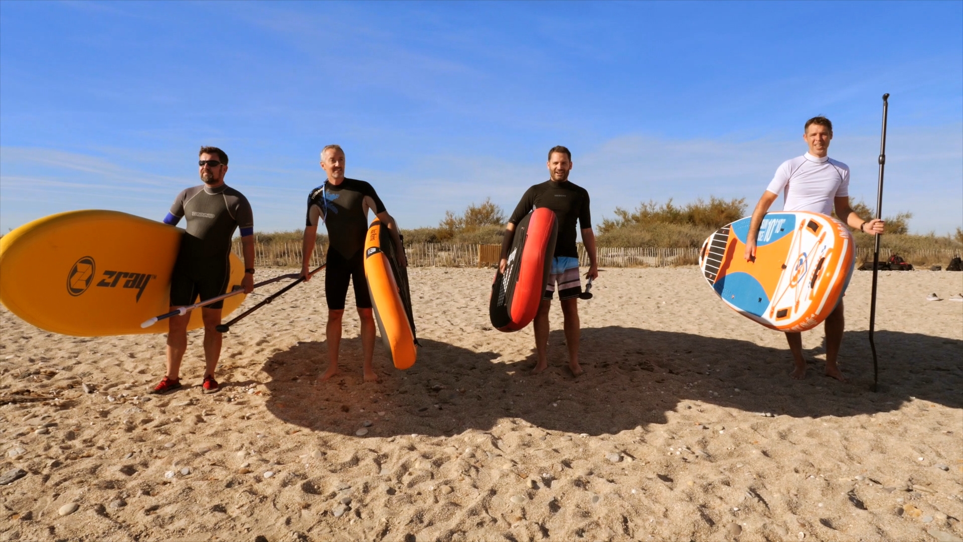 4 copains se préparent sur la plage à faire du paddle