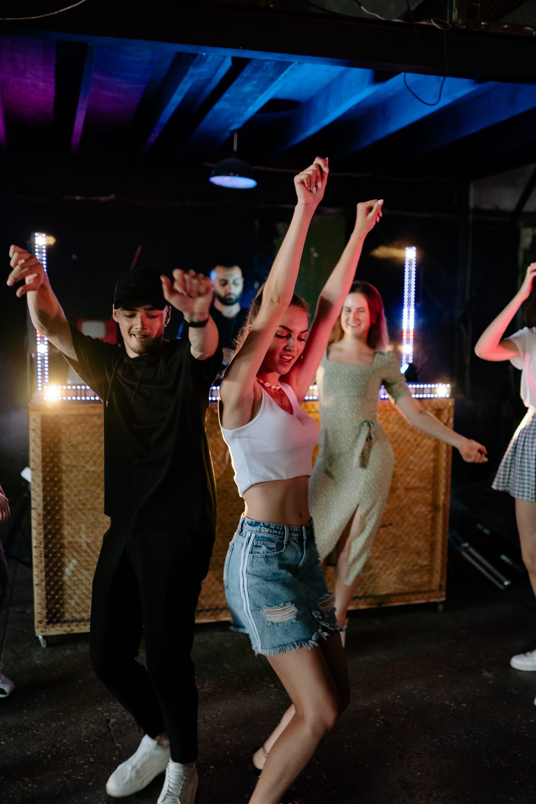 Jeune home et jeune fille, bras levés en train de danser. DJ en arrière plan.