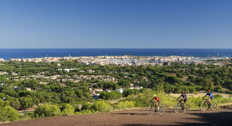 Trois hommes gravissent le mont Saint Loup en VTT avec superbe vue sur le port du Cap d'Agde et la mer Méditerranée