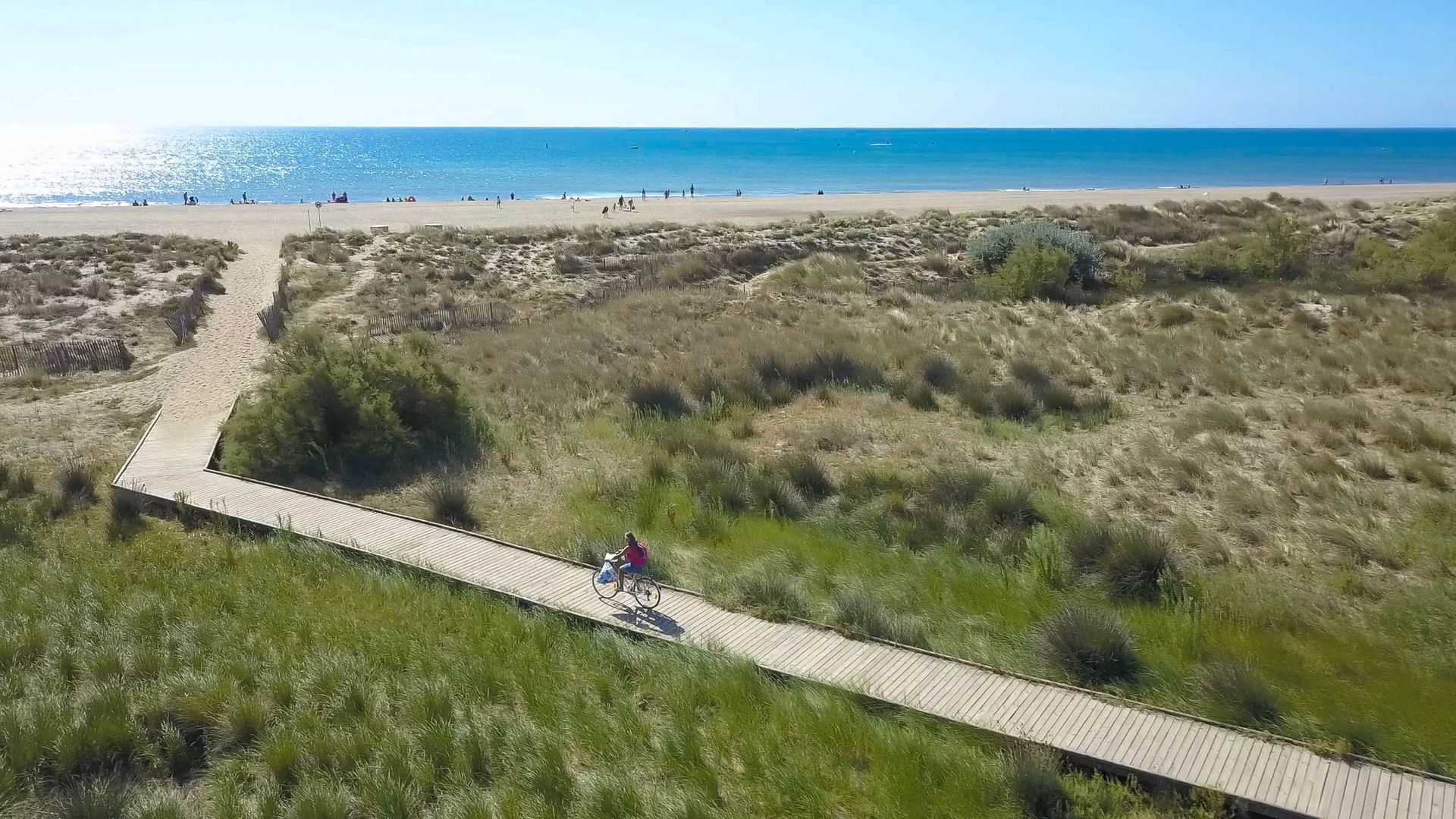 Une femme arrive en vélo à la plage de Vendres via un platelage en bois