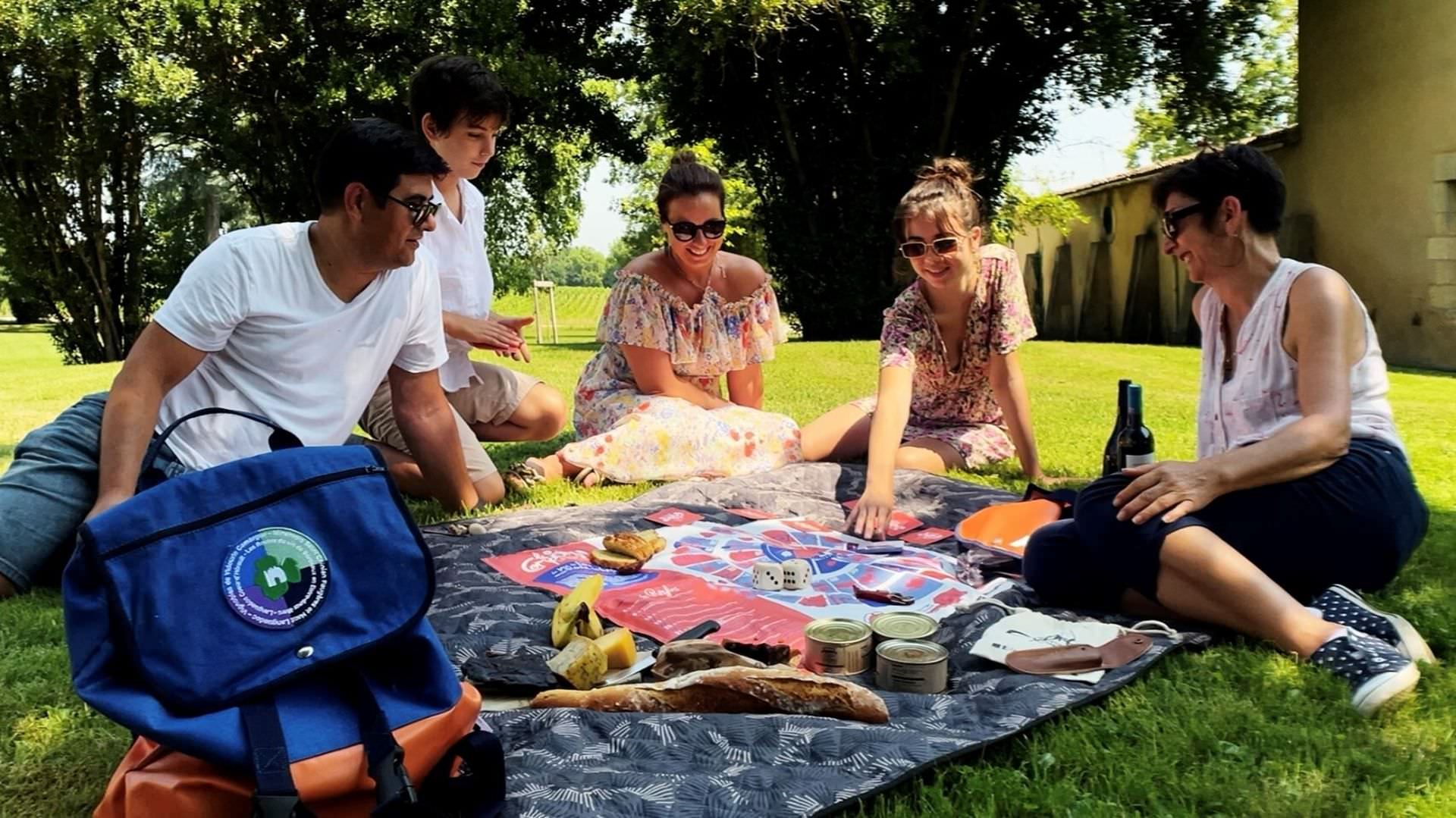 Une famille joue et pique-nique sur l'herbe dans un domaine viticole qui propose Le Comporte, sac à dos vigneron, en Languedoc Coeur d'Hérault