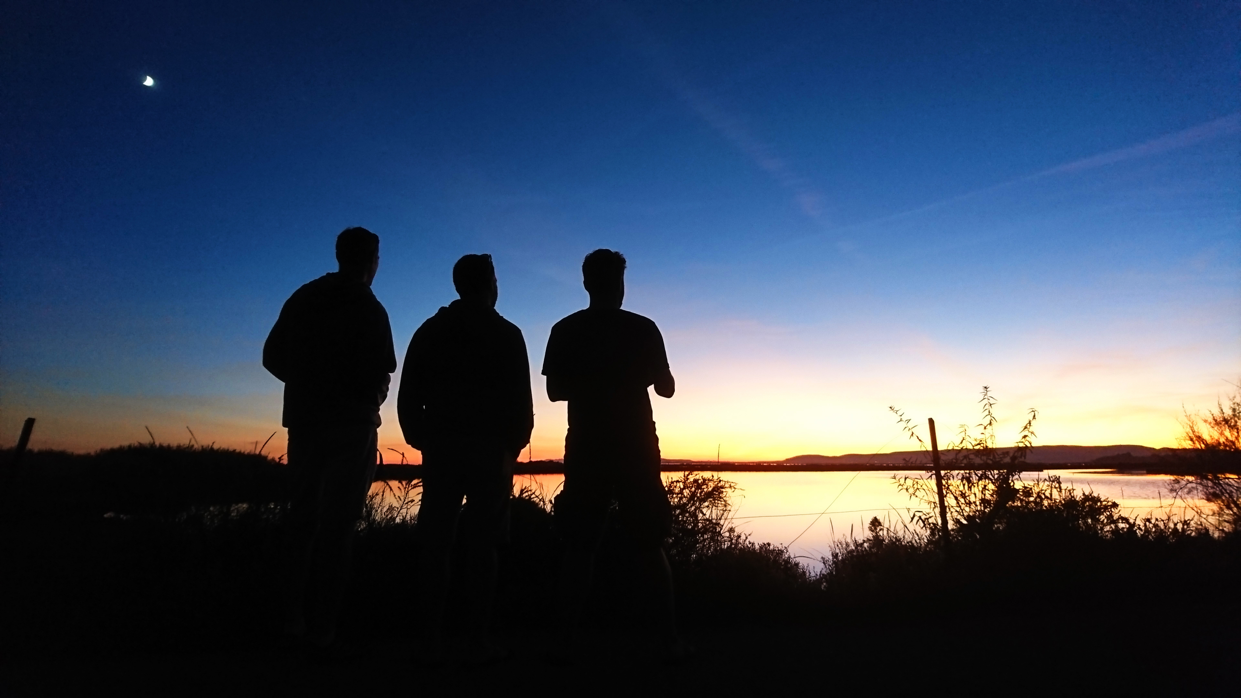 3 hommes de dos, regardent le coucher du soleil sur les étangs