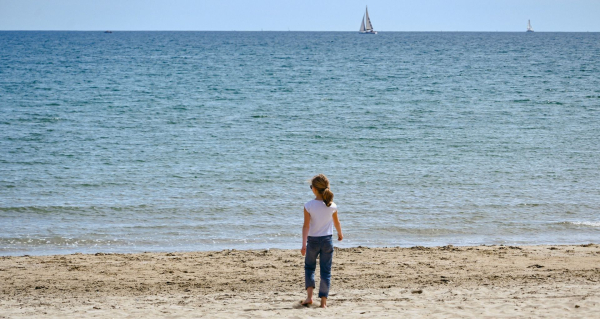 Une jeune fille se promène sur la plage de Palavas-Les-Flots, rive gauche, et observe les bateaux naviguer sur l'eau au loin