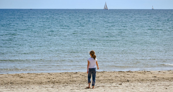 Une jeune fille se promène sur la plage de Palavas-Les-Flots, rive gauche, et observe les bateaux naviguer sur l'eau au loin