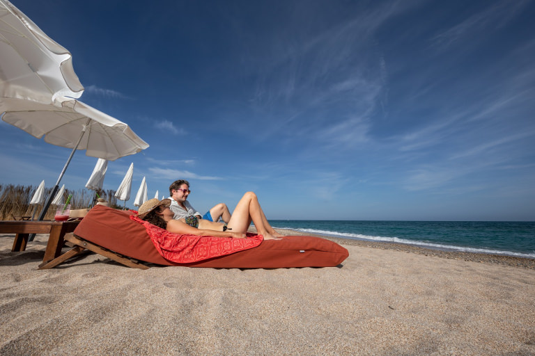 Plage privée Carré Mer © Anthony Alliès 2 personnes sont allongées face à la mer sur des canapés posés sur le sable.