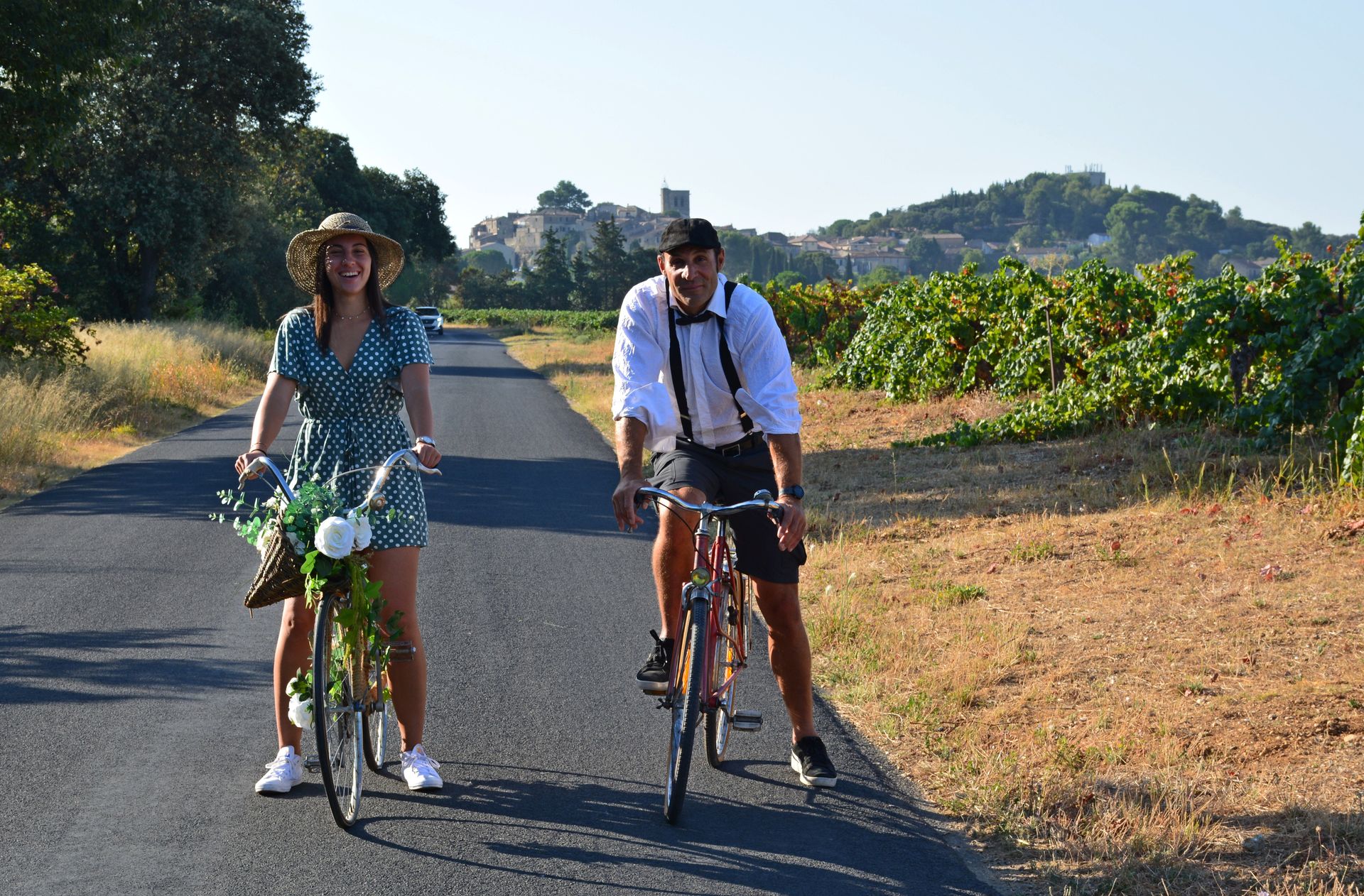 Un homme et une femme se baladent en vélo vintage le long des vignes près du village du Pouget dans le cadre de l'évènement Musette & Bicyclette de Fascinant Week-end