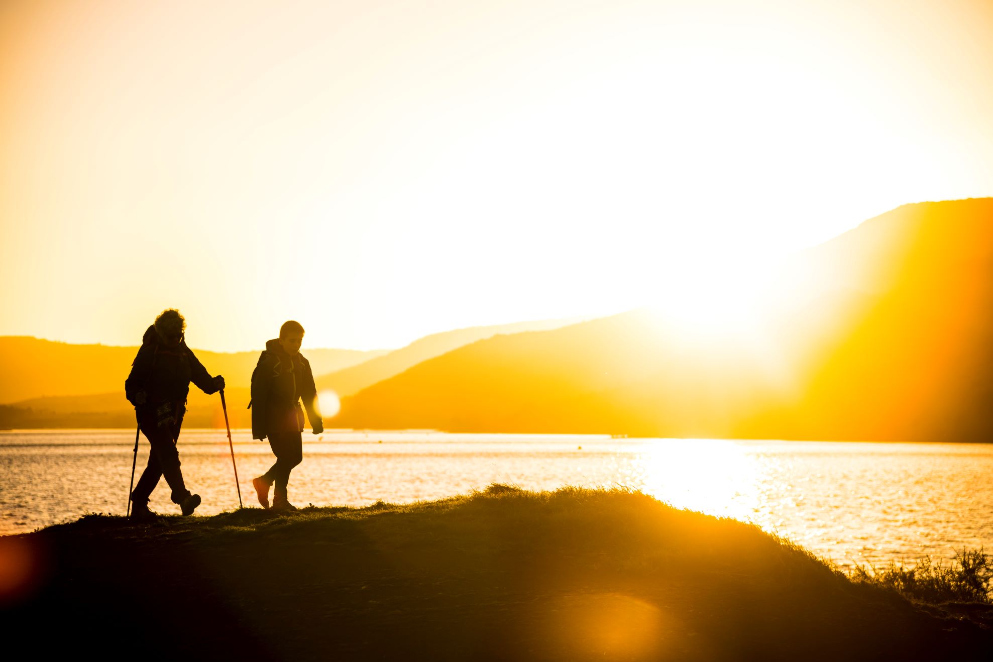 Deux hommes terminent leur randonnée autour du lac du Salagou à la tombée de la nuit. Le jaune du soleil pâlit et reste éblouissant.