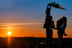 Un jeune couple avec leurs enfants se promènent au coucher de soleil sur le sable avec un cerf volant