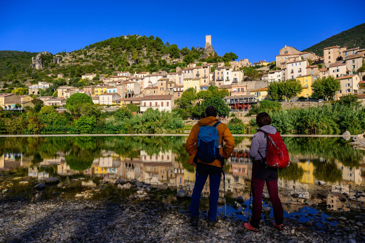 Un couple de randonneur admire le village de Roquebrun dans le Haut-Languedoc depuis les berges de l'Orb