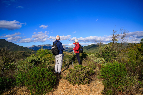 Un couple randonne sur le PR de l'Ayrolle entre vignes et montagnes du Caroux à l'automne