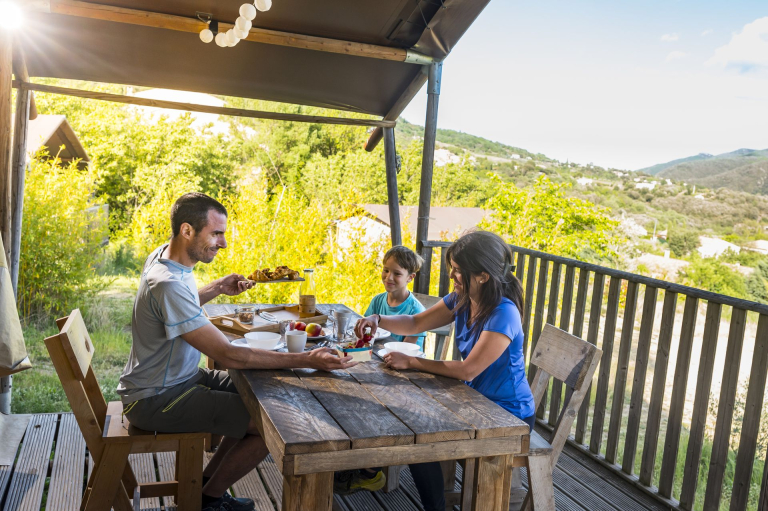 Une famille prend son petit-déjeuner sur la terrasse du tente lodge au Camping du Caroux dans le Haut-Languedoc