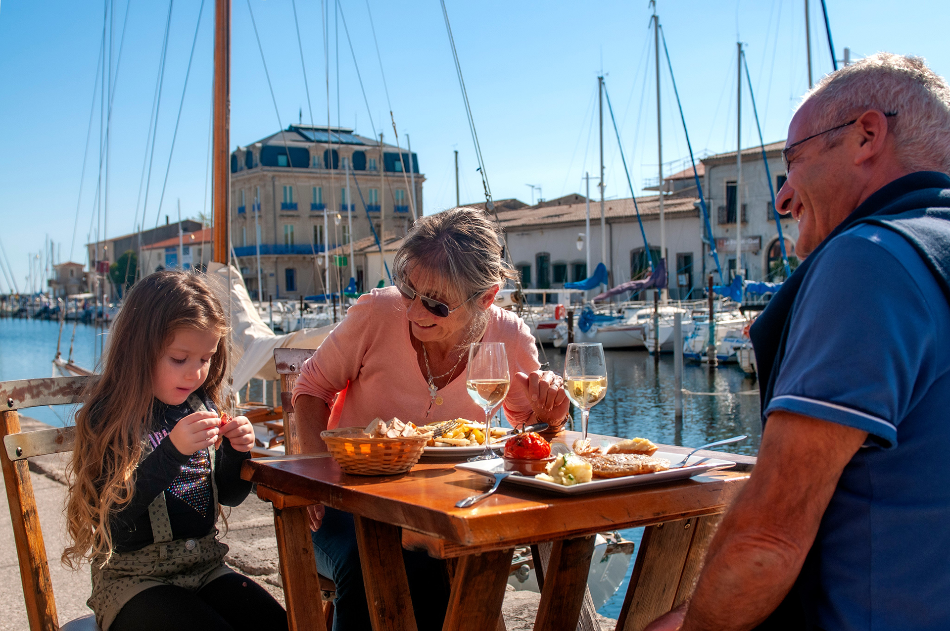 Couple de jeuniors qui mange en terrasse au restaurant sur le port de Marseillan avec leur petit fille en famille