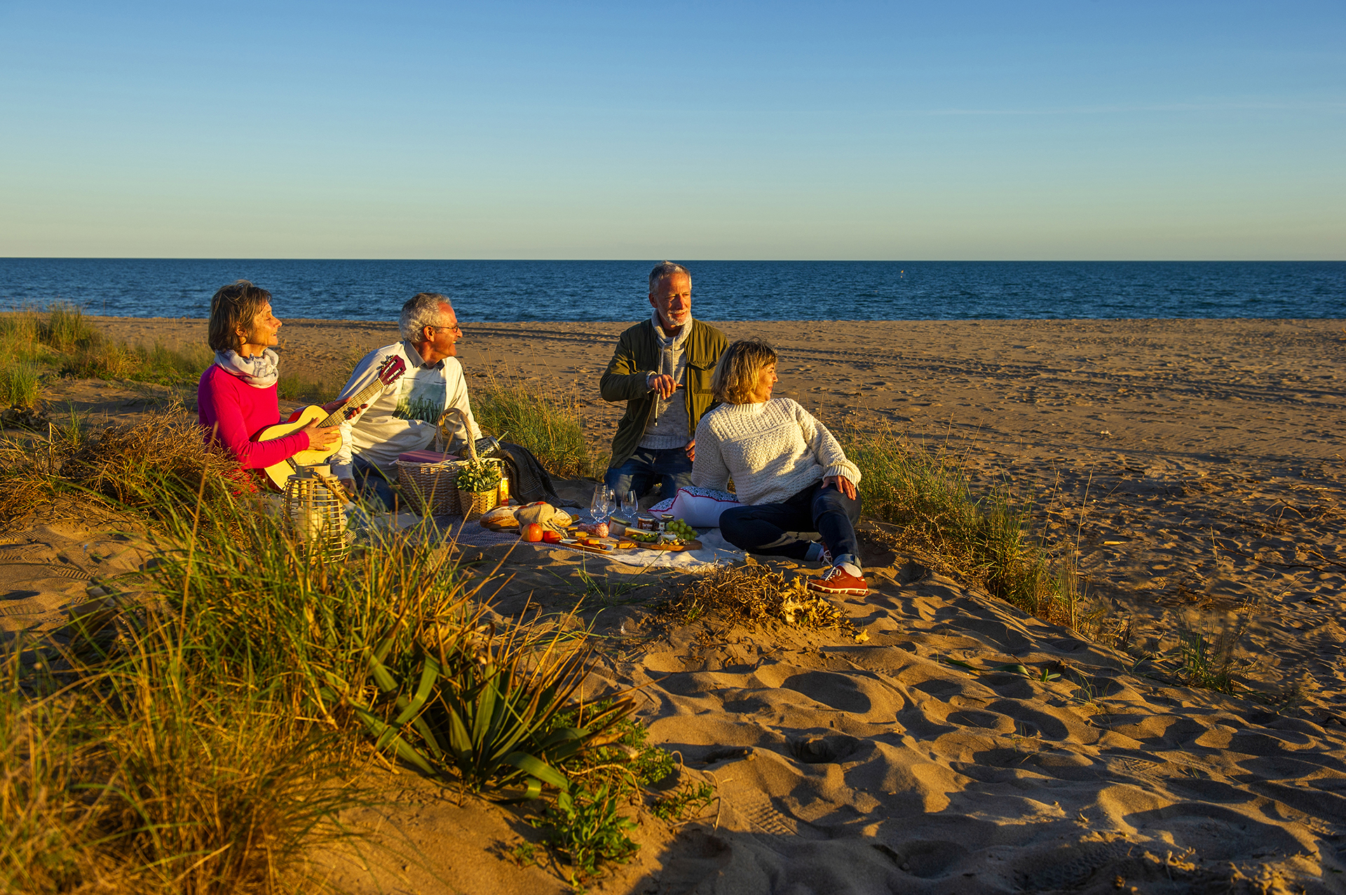 Groupe d'amis jeuniors qui pique niquent sur la plage de Portiragnes au coucher du soleil