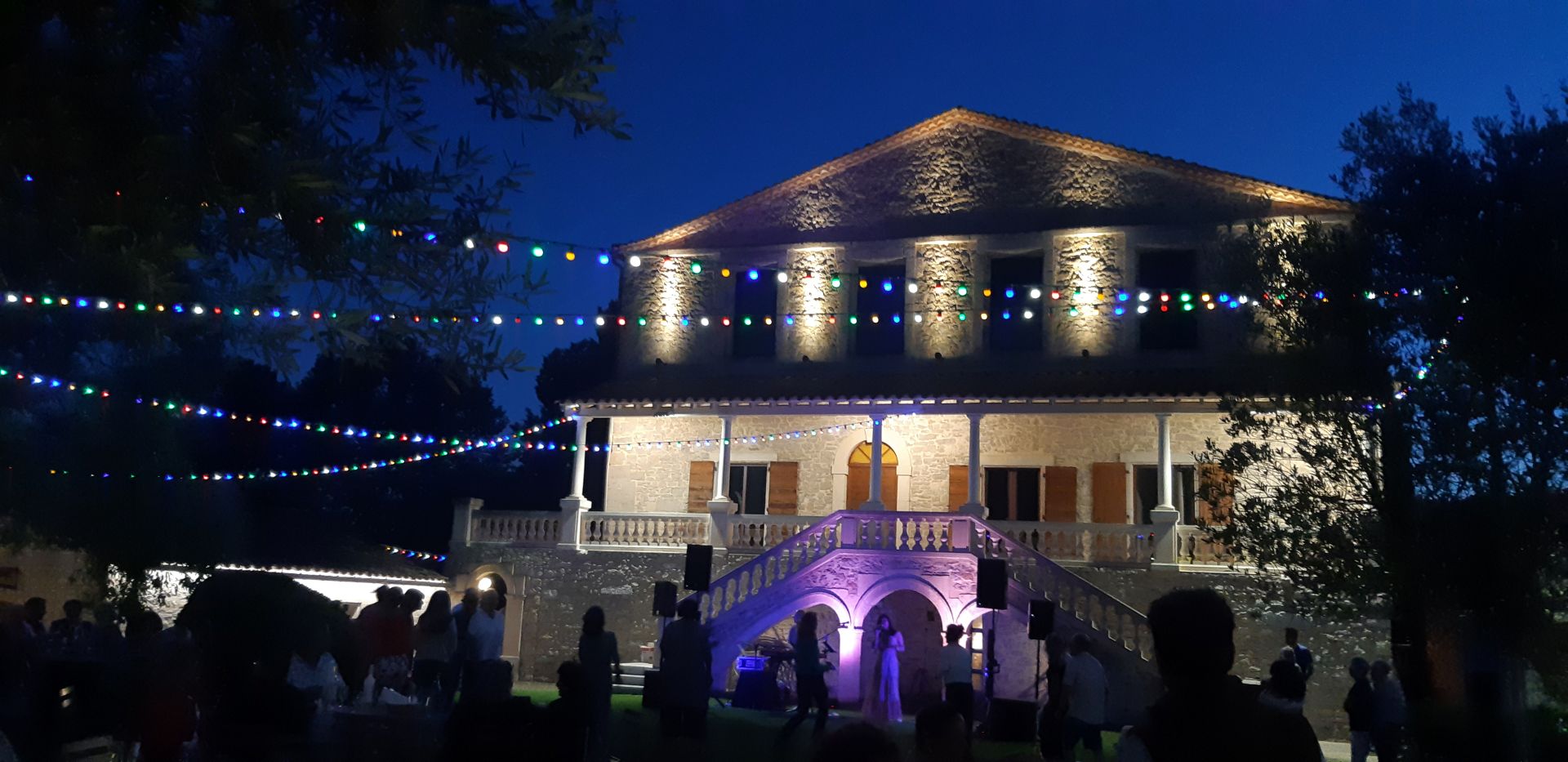Dans la nuit à la lumières multicolore des guirlandes dans gens dansent au son d'un groupe devant la demeure du Château La Roque.