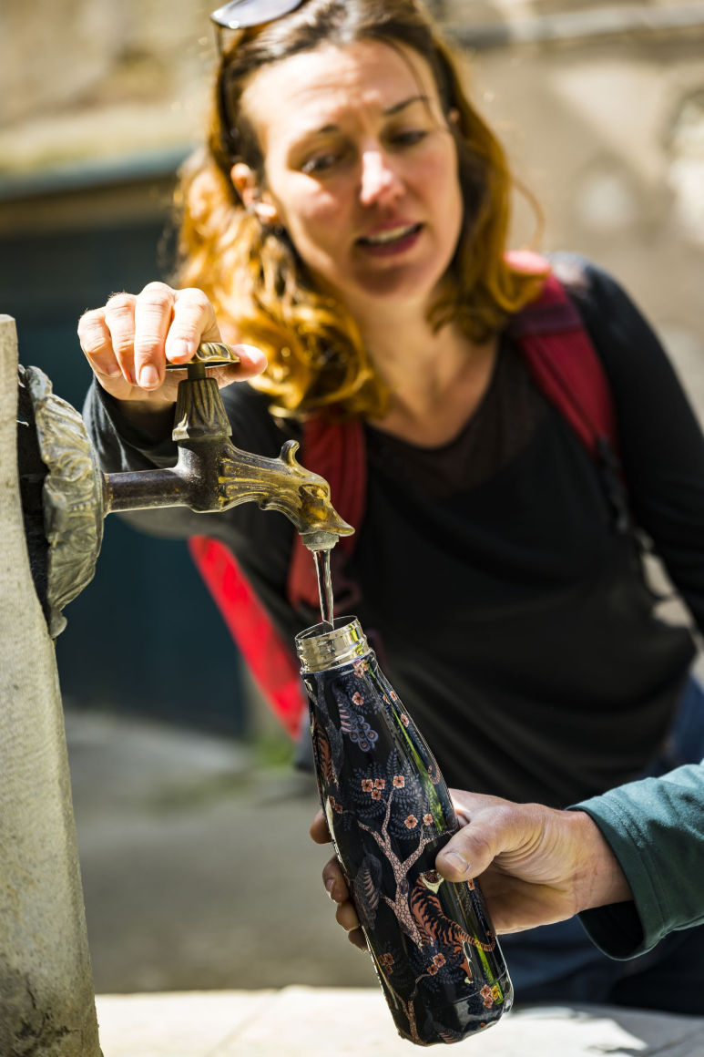 Une femme remplit une gourde d'eau potable à la fontaine d'un village de l'Hérault