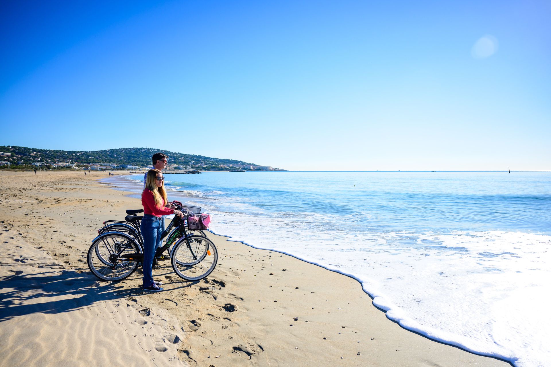 Un couple avance sur la plage du Lido de Sète àavec leurs vélos